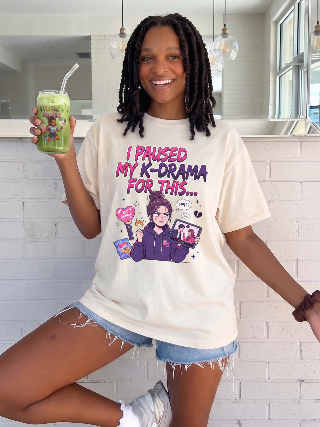 Young woman wearing The K&C Fangirl "I Paused My K-Drama For This" Sarcastic K-Drama Fangirl Vintage Cream Oversized Tee while drinking an iced matcha in can shaped glass